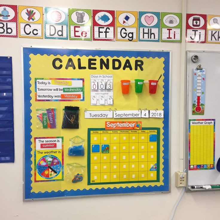 a bulletin board with calendars, cups and magnets on it in a classroom