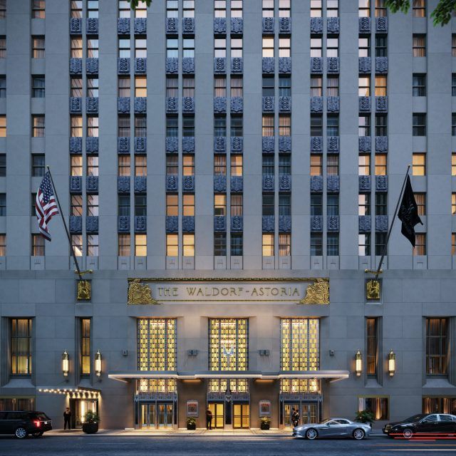 the front entrance of an art deco hotel at night with cars parked in front and lights on