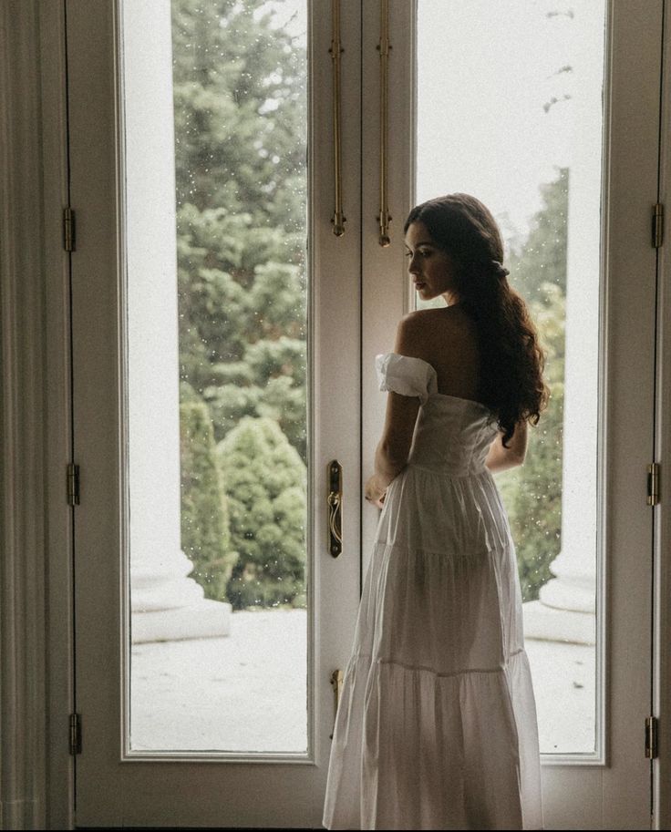 a woman standing in front of a door wearing a white dress