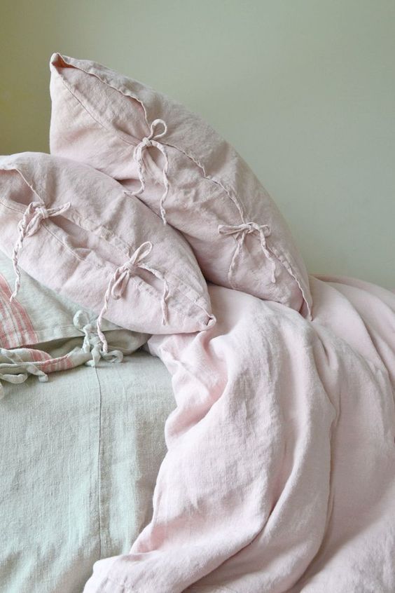 an unmade bed with pink linens and pillows on top of it, next to a white wall