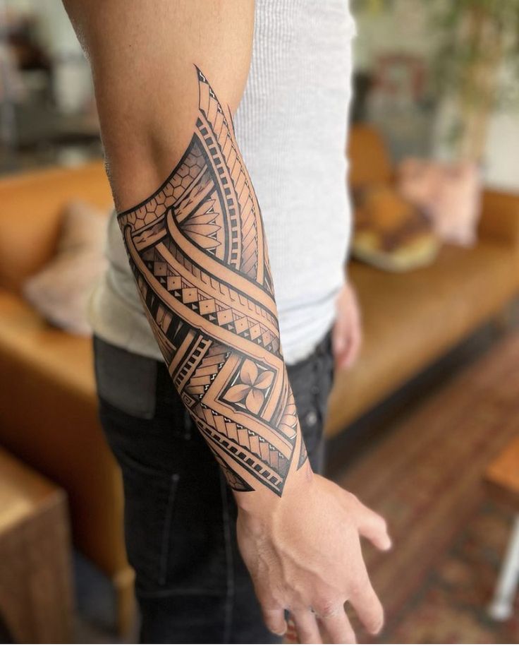 a man with a tattoo on his arm and hand is standing in front of a couch