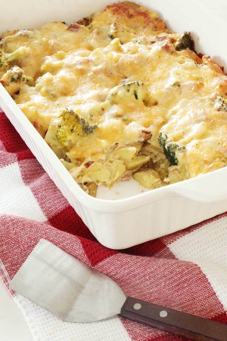 a casserole dish with broccoli and cheese in it next to a knife