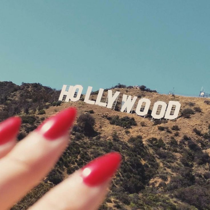 a woman's hand with red nail polish holding up the hollywood sign