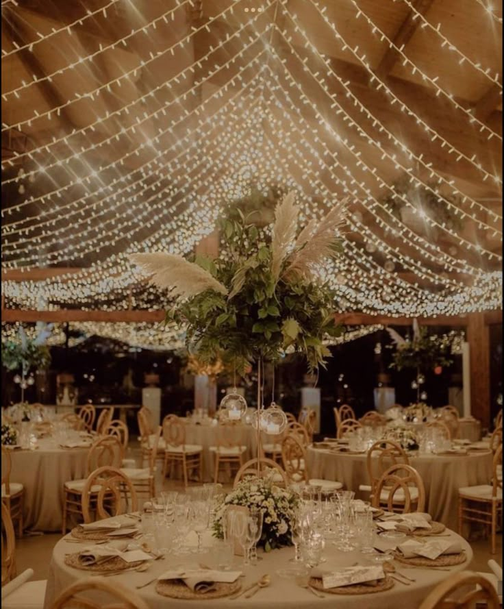 the tables are set up for an event with white linens and lights strung overhead