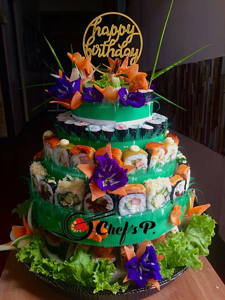 a three tiered cake decorated with sushi and lettuce is displayed on a table