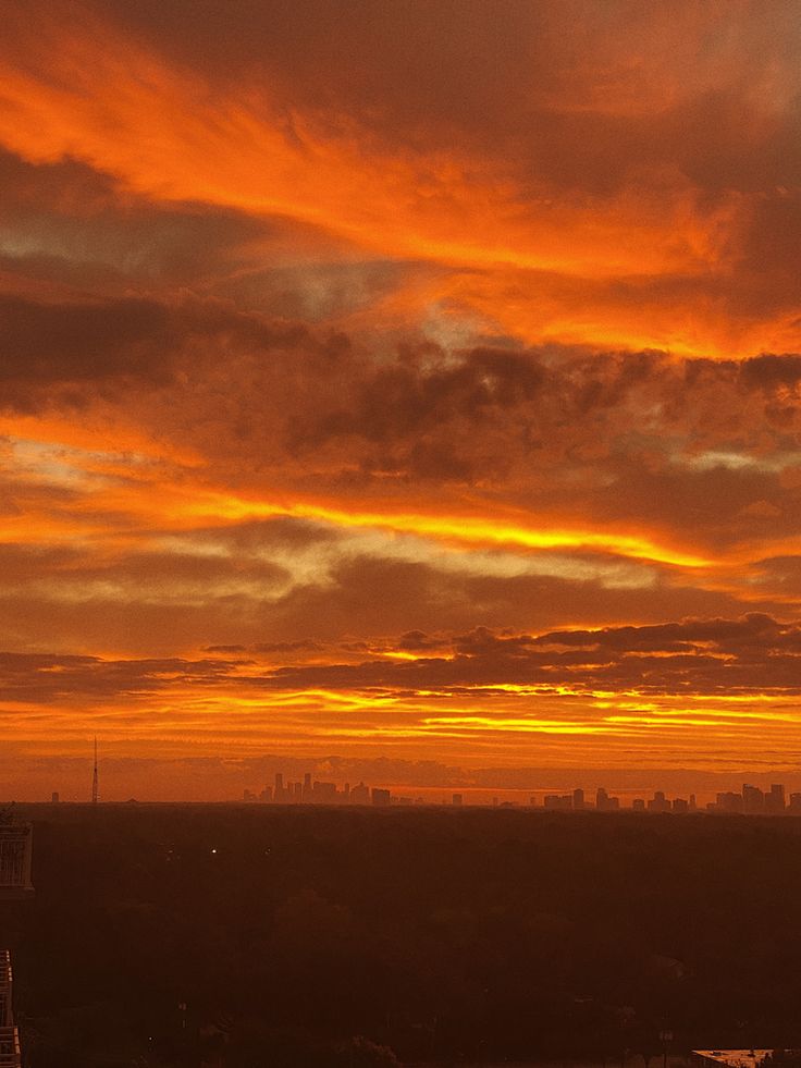 an orange and yellow sky with clouds over a city