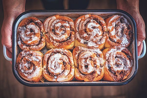 a person holding a pan filled with cinnamon rolls