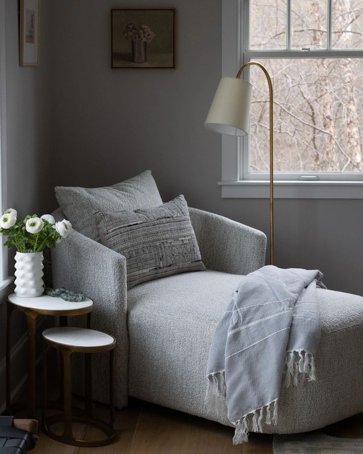 a living room with a chair, lamp and flowers on the table in front of it