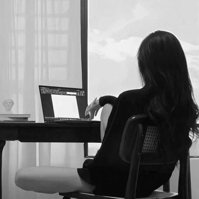 a woman sitting at a desk with a laptop in front of her, looking out the window