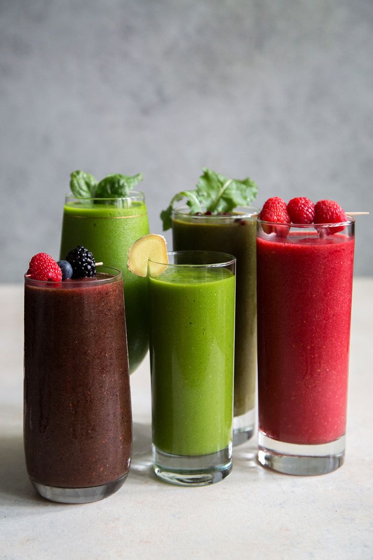 three smoothies are lined up on a table with raspberries and spinach