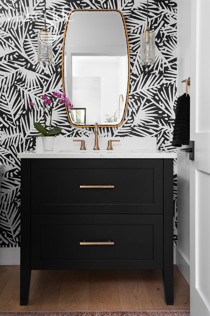 a bathroom with black and white wallpaper, gold accents and a large mirror above the sink