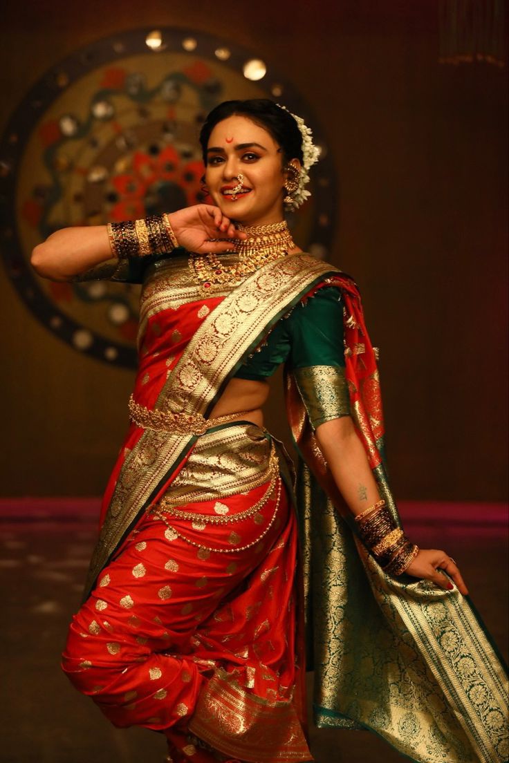 a woman in a red and gold sari dancing with her hand on her hip