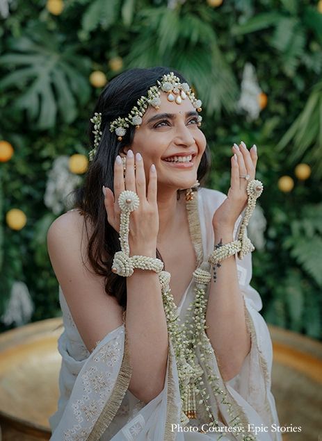 a woman in a white dress is holding her hands up to her face and smiling