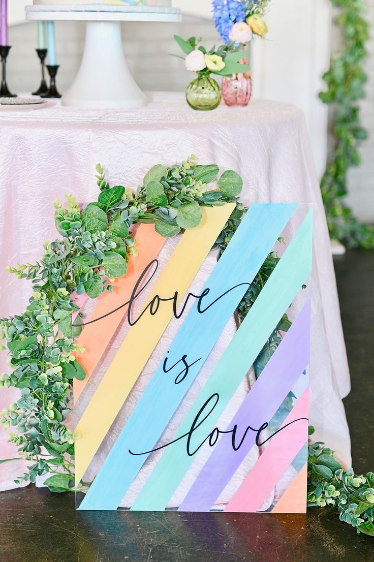 a colorful sign that says love is love on top of a table with greenery