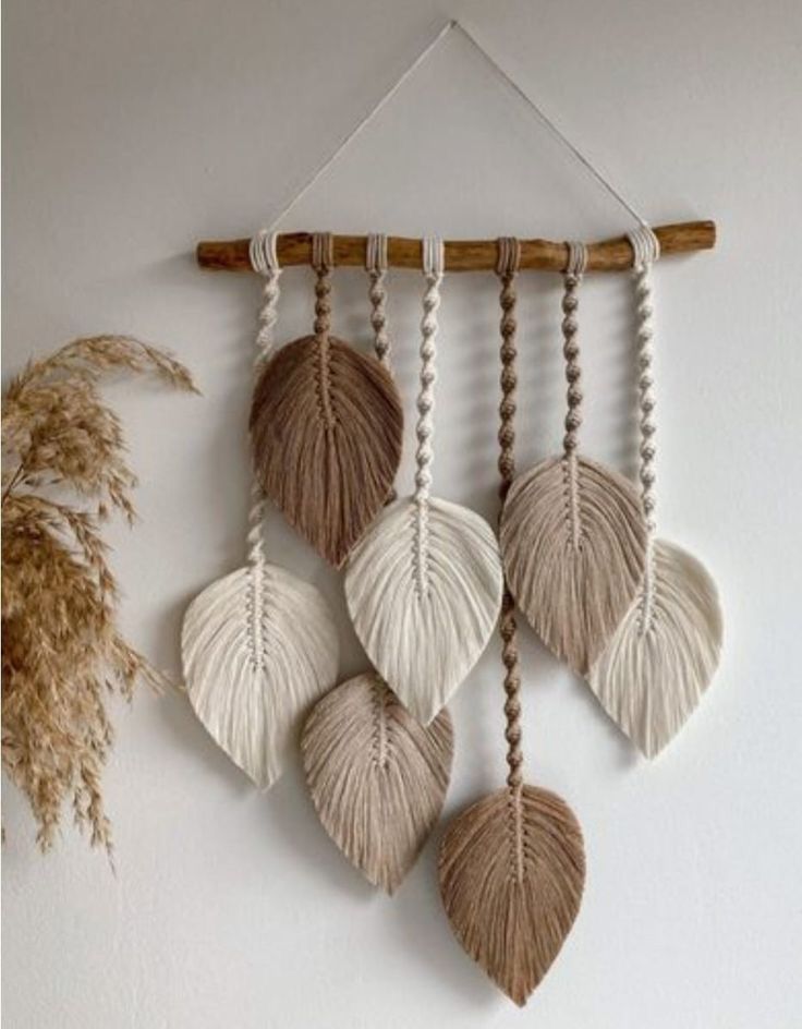 a wall hanging made out of shells and rope with some dried plants in the background