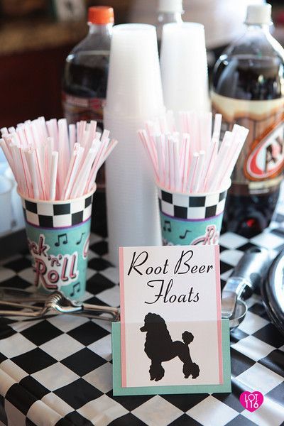 a table topped with cups filled with pink and white straws next to bottles of soda