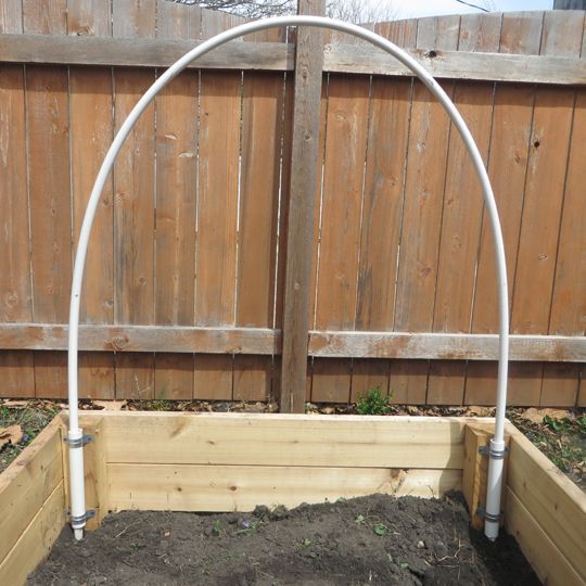 an empty garden bed in front of a wooden fence with metal piping on it