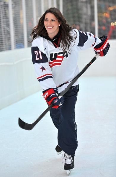 a woman is playing hockey on an ice rink and smiling at the camera with her stick