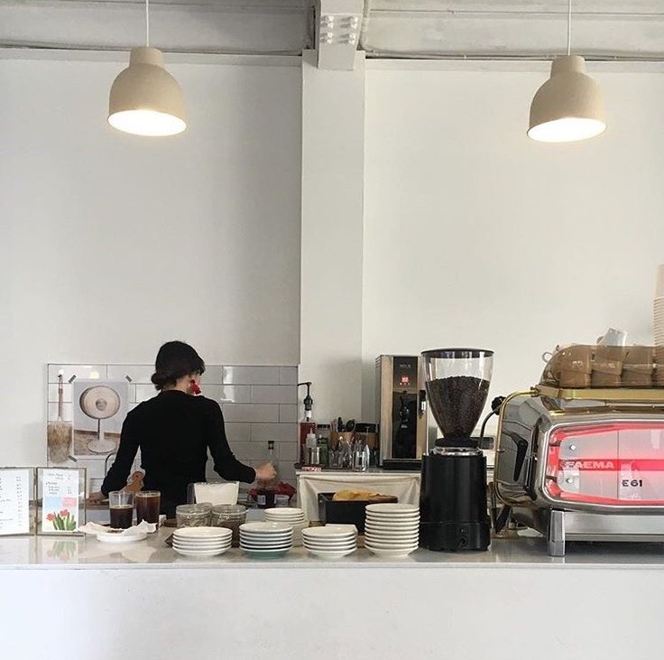 a woman standing behind a counter filled with plates and coffee cups next to an espresso machine