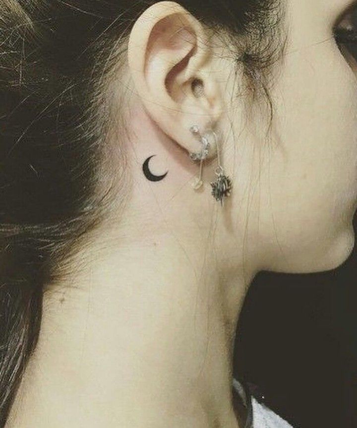 a woman's ear with a small crescent tattoo on it