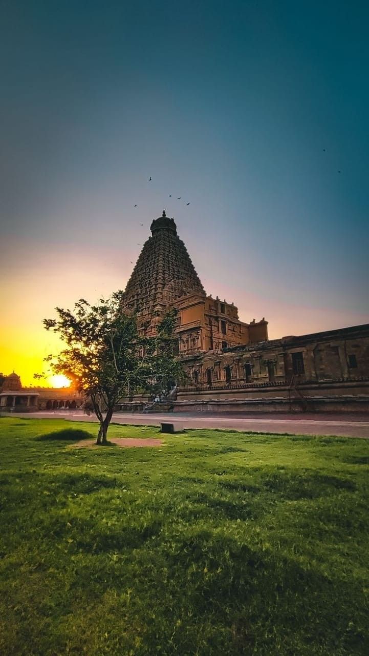 the sun is setting in front of an old building with a tree on the lawn