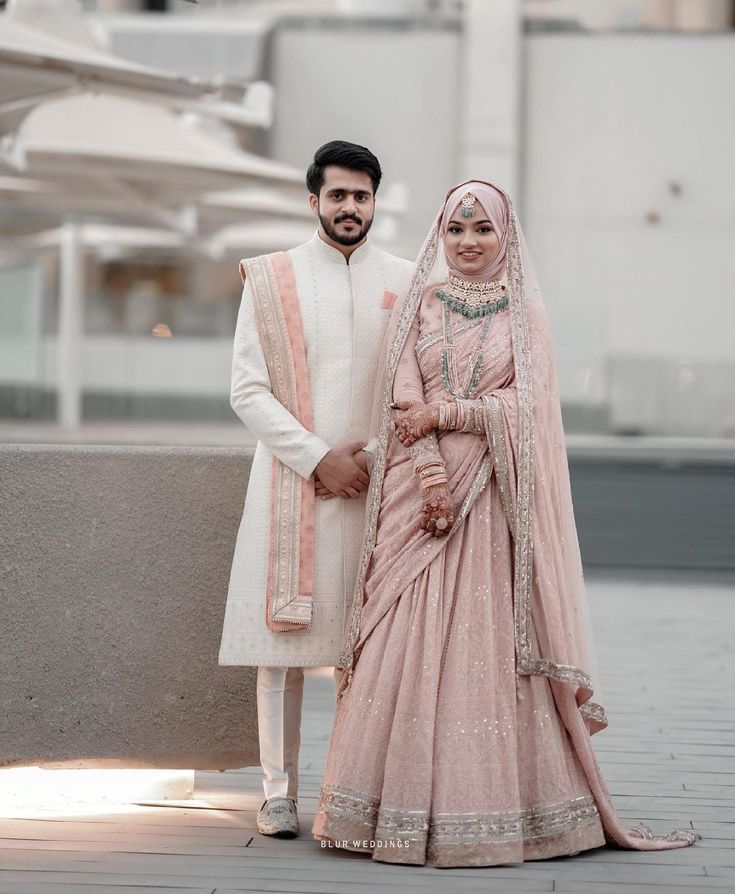 two people standing next to each other wearing wedding outfits and posing for the camera in front of a building