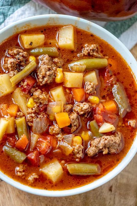 a white bowl filled with meat and vegetable soup on top of a wooden table next to a spoon