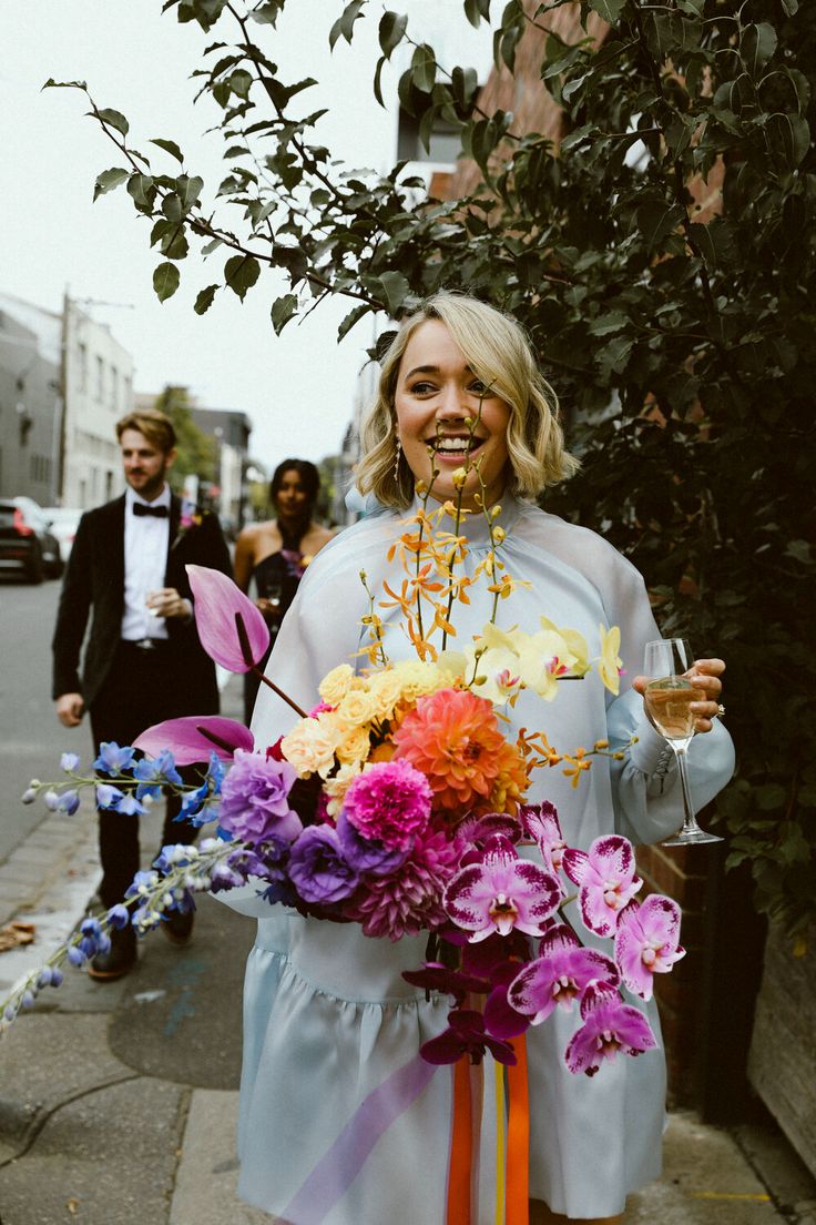 a woman holding a bunch of flowers in her hands while standing on the side walk