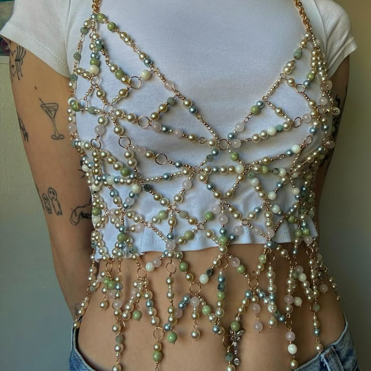 new proj! dm to chat about customs 🩵 perfect for summer over a lil t-shirt or tank top, fun little festival top as pieces move while you dance and just sexc period what can i sayyyyyyy entirely made with gold eyepins + jump rings, variety of pearl beads, gold beads, and natural stone beads, along with gold chain & gold clasps! this was entirely an unplanned project but i’m ecstatic with how it turned out. procrastinating studying for a couple days got me to make this so really procrastinat... Clothes With Pearls, Bead Embroidery Tank Top, Diy Bejeweled Top, Beaded Harness Diy, Diy Festival Accessories, Beaded Tank Top, Chain Top Outfit, Beaded Top Diy, Custom Diy Ideas