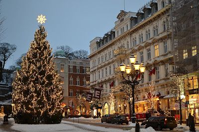 a christmas tree is lit up in the middle of a snowy city street at night