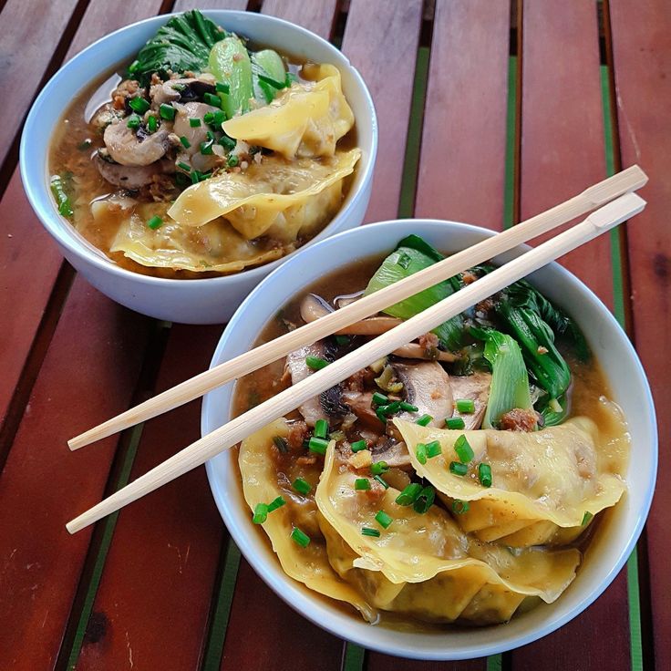 two bowls filled with food and chopsticks on top of a wooden table next to each other