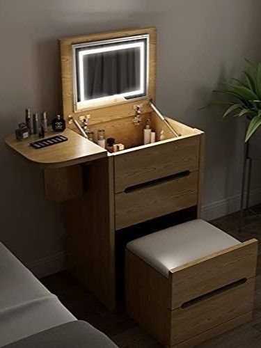 a small wooden vanity with a mirror and stool in the corner next to a bed