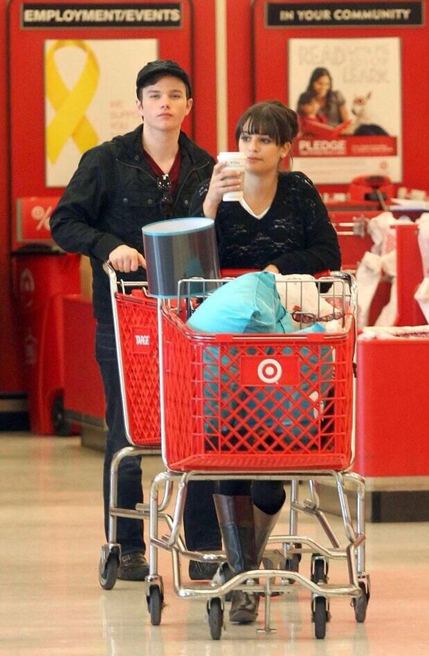 a man and woman are sitting in a shopping cart at the grocery store, one is holding a cup