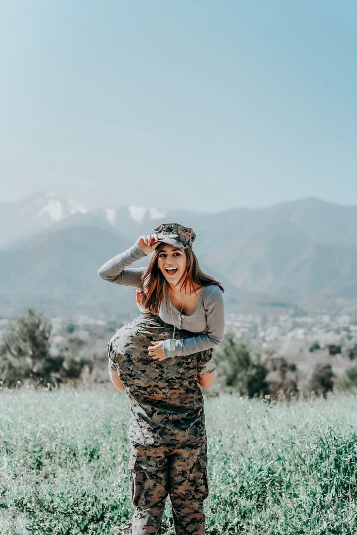 a woman in camo pants and a gray sweater is holding her baby on her back