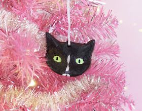 a black cat ornament hanging from a pink christmas tree