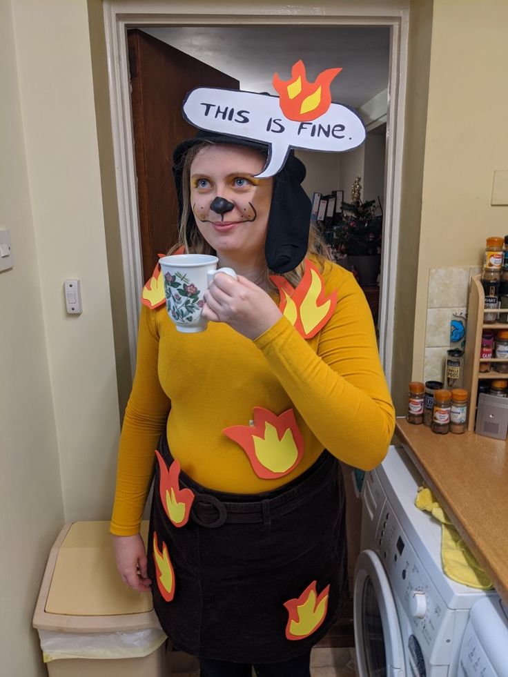 a woman in a costume holding a cup and wearing a funny hat with the words this is fine on it