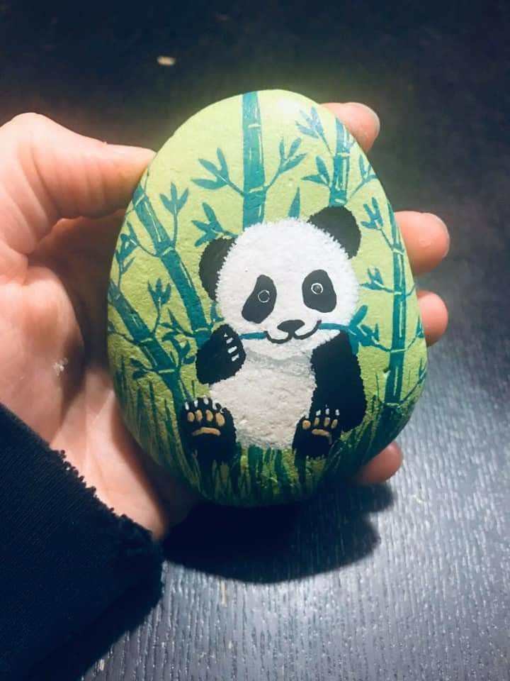 a hand holding a painted rock with a panda bear on it