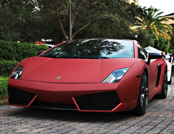 a red sports car parked on the side of a road next to some bushes and trees