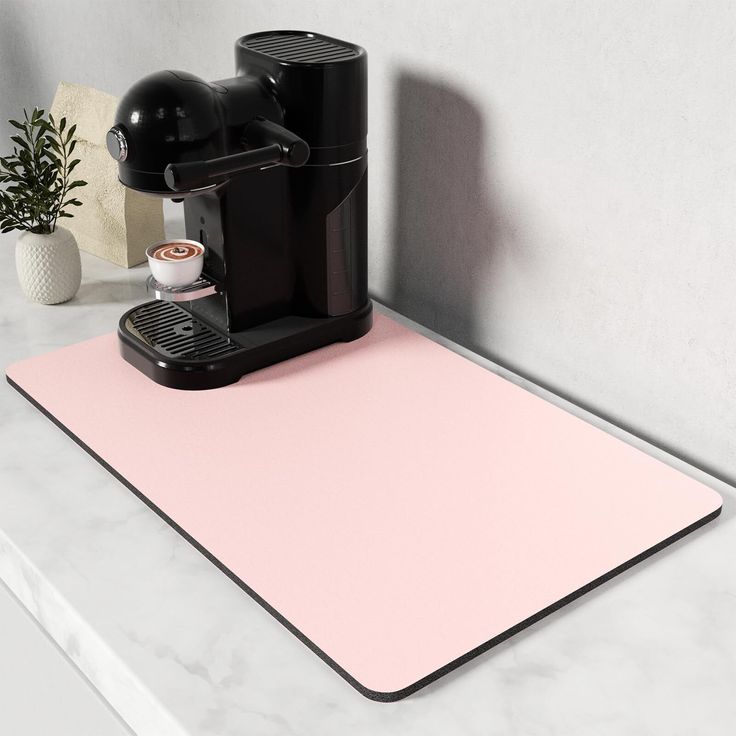 a coffee maker sitting on top of a counter next to a pink mat and potted plant