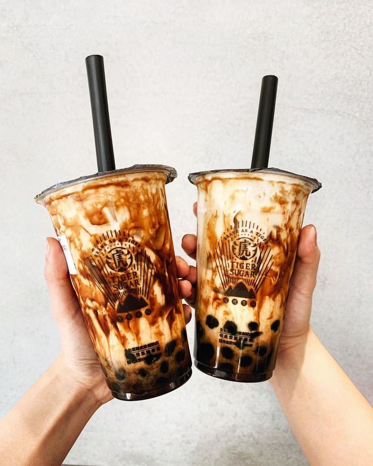 two people holding up cups with drinks in them, one is brown and the other has black straws