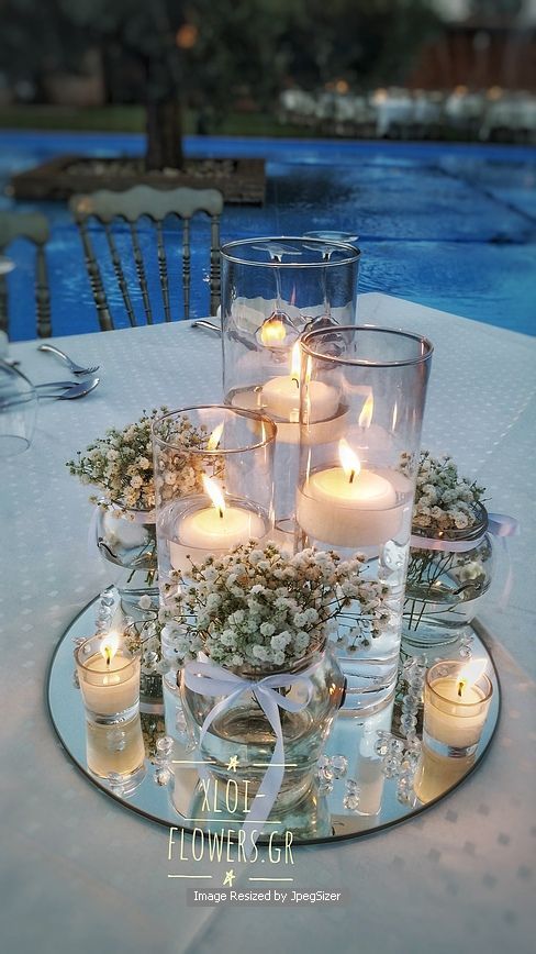 a table with candles and flowers on it next to a swimming pool in the background