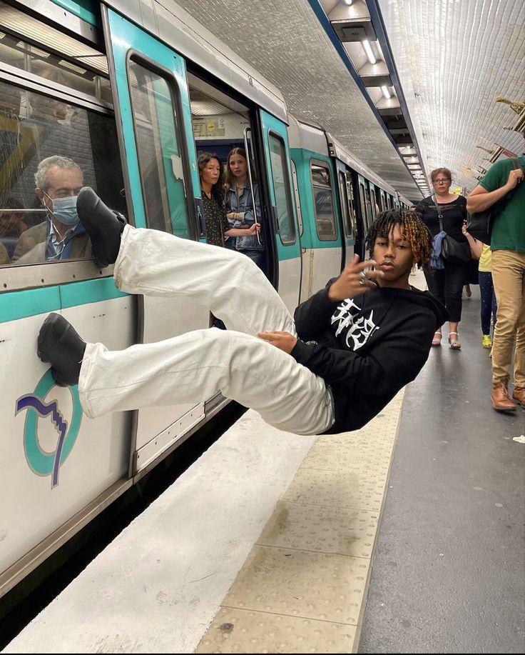 a man is hanging off the side of a subway train while people are waiting for it