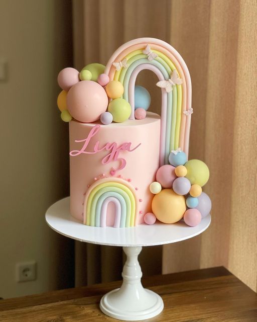 there is a pink cake with rainbow decorations on the top and letters that spell it