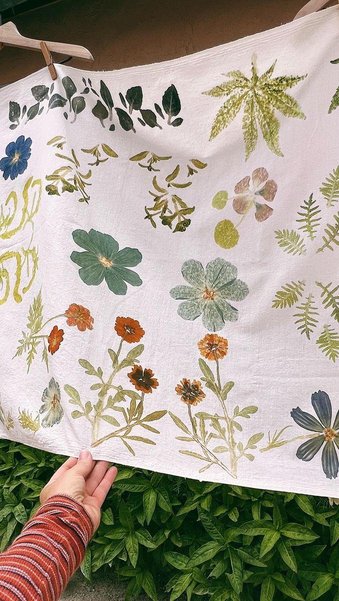 a person holding up a white cloth with flowers on it in front of some bushes