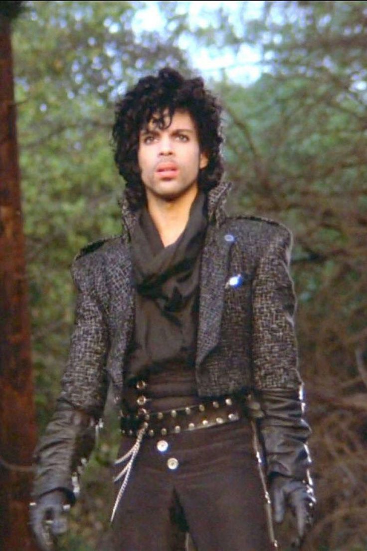 a young man with black hair and leather gloves on his head, wearing a jacket