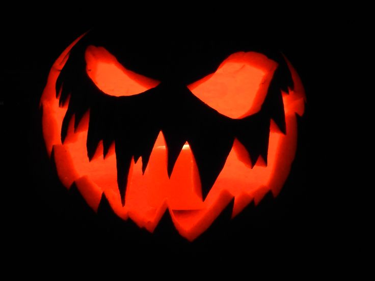 a carved pumpkin with sharp teeth on it's face, lit up in the dark