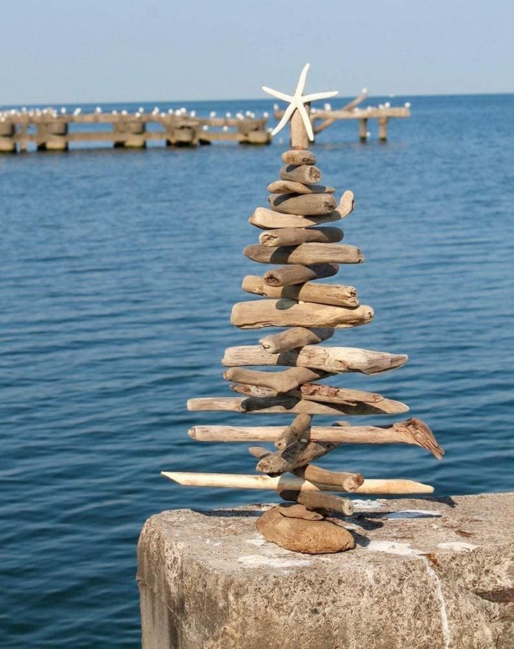 a rock christmas tree sitting on top of a stone wall next to the ocean and pier