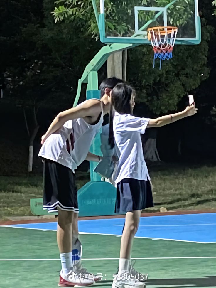 two young people playing basketball on an outdoor court