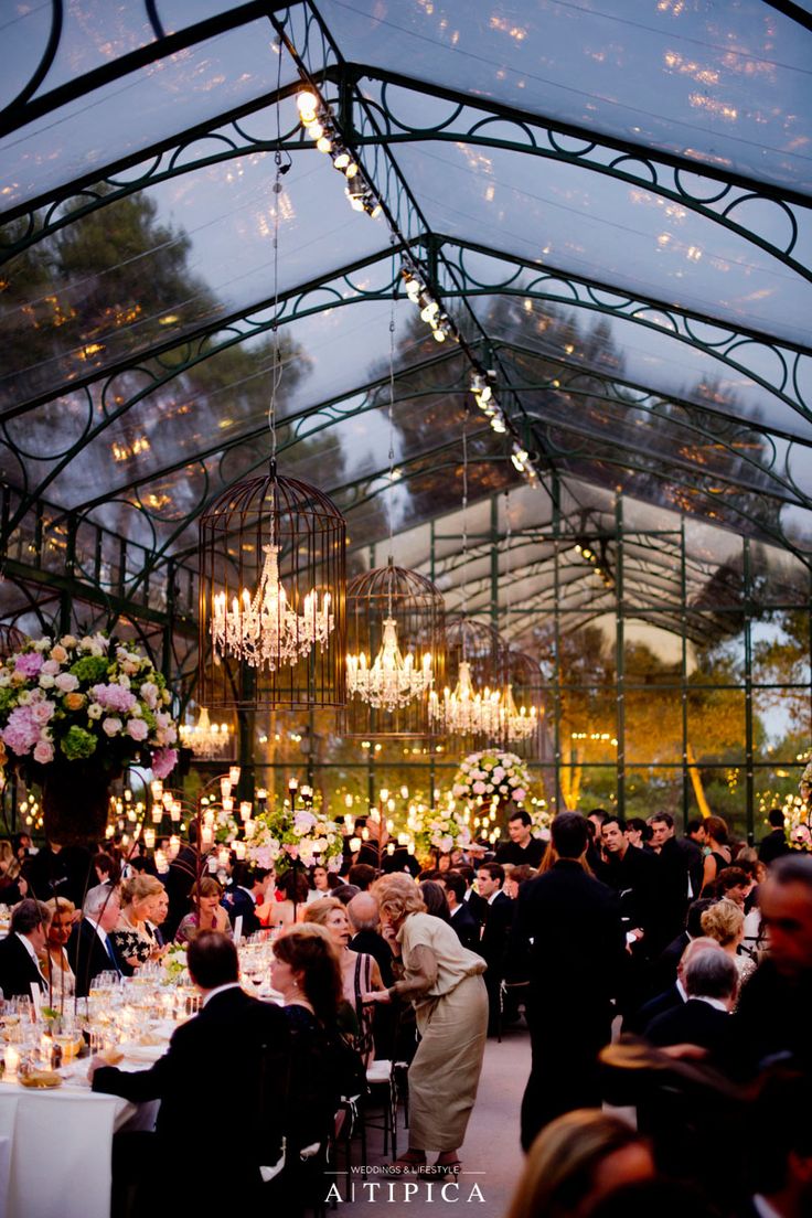 a large group of people sitting at tables in a room with chandeliers hanging from the ceiling