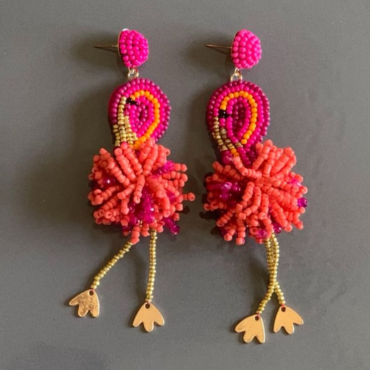 two pairs of pink and orange beaded earrings with dangling hooks on grey surface,